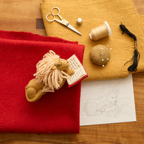 The design process for a handmade felt ornament of a wise lion wearing tiny felt glasses, absorbed in a large red book. Crafted from natural wool, this charming lion adds a storybook touch to holiday trees, reading nooks, or cozy corners. A delightful gift for readers, teachers, librarians, or anyone who loves books and imagination. Each ornament is unique, crafted with care using traditional felting techniques.