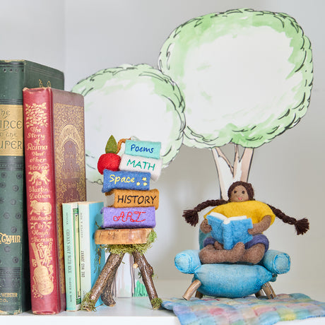 Handmade felt ornament of a young girl sitting cross-legged, absorbed in a book. Crafted from natural merino-blended wool, her focused gaze and relaxed posture capture the magic of reading. With braided brown hair and a warm-toned complexion, this ornament adds a cozy, literary touch to reading nooks, desks, or shelves. A perfect gift for bookworms, young readers, or anyone who treasures the quiet joy of a good story. Ready to hang with a string attached.