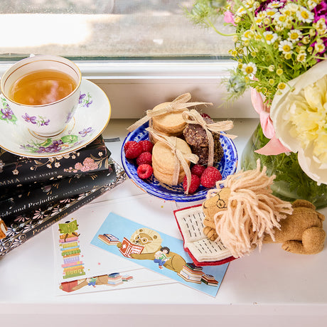A glasses  wearing reading lion, part of the Reading-themed gift bundle featuring four handmade wool felt ornaments—a gnome reading a book, a lion with glasses holding a book, a young girl reading, and a fairy with wings reading—alongside a coordinating stationery set. Stationery includes a notepad, four illustrated notecards with envelopes, and four colorful bookmarks, all featuring characters from the Reading Collection. Ornaments are made from natural merino-blend wool and come ready to hang.