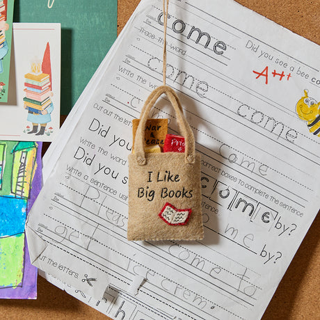Handmade felt ornament shaped like a tote bag filled with miniature felt books, including titles like Pride & Prejudice and War & Peace. Crafted from soft merino-blended wool, this quirky ornament is a playful nod to literary humor. Perfect for bookworms, teachers, librarians, and pun enthusiasts, it adds a clever touch to holiday trees, bookshelves, or classrooms. Ready to hang with a string attached.