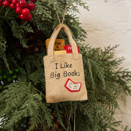 Handmade felt ornament shaped like a tote bag filled with miniature felt books, including titles like Pride & Prejudice and War & Peace. Crafted from soft merino-blended wool, this quirky ornament is a playful nod to literary humor. Perfect for bookworms, teachers, librarians, and pun enthusiasts, it adds a clever touch to holiday trees, bookshelves, or classrooms. Hanging from a Chrismas tree