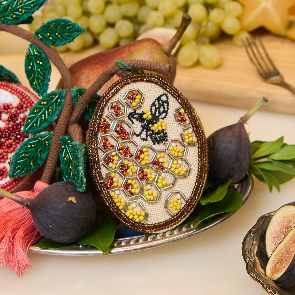 Fair trade beehive ornament featuring delicate beadwork and embroidered bee in flight