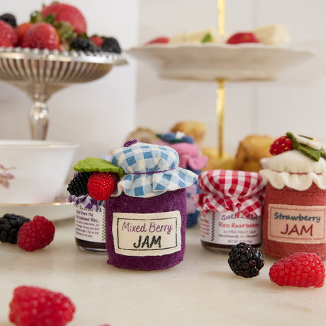 Hand-felted wool ornament of a berry jam jar with a red gingham-patterned lid, topped with beaded blackberry and raspberry accents. Crafted with embroidered details and soft textures, it includes a hanging string and measures approximately 2.75 inches high. A sweet, handmade tribute to homemade preserves and cozy kitchen moments.
