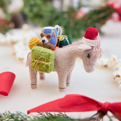 Handmade felt Donkey with Gifts ornament from Craftspring, wearing a Santa hat and carrying toys—displayed among evergreens and a popcorn garland, perfect for Christmas gifting and festive decor, ethically crafted by artisans using sustainable wool.