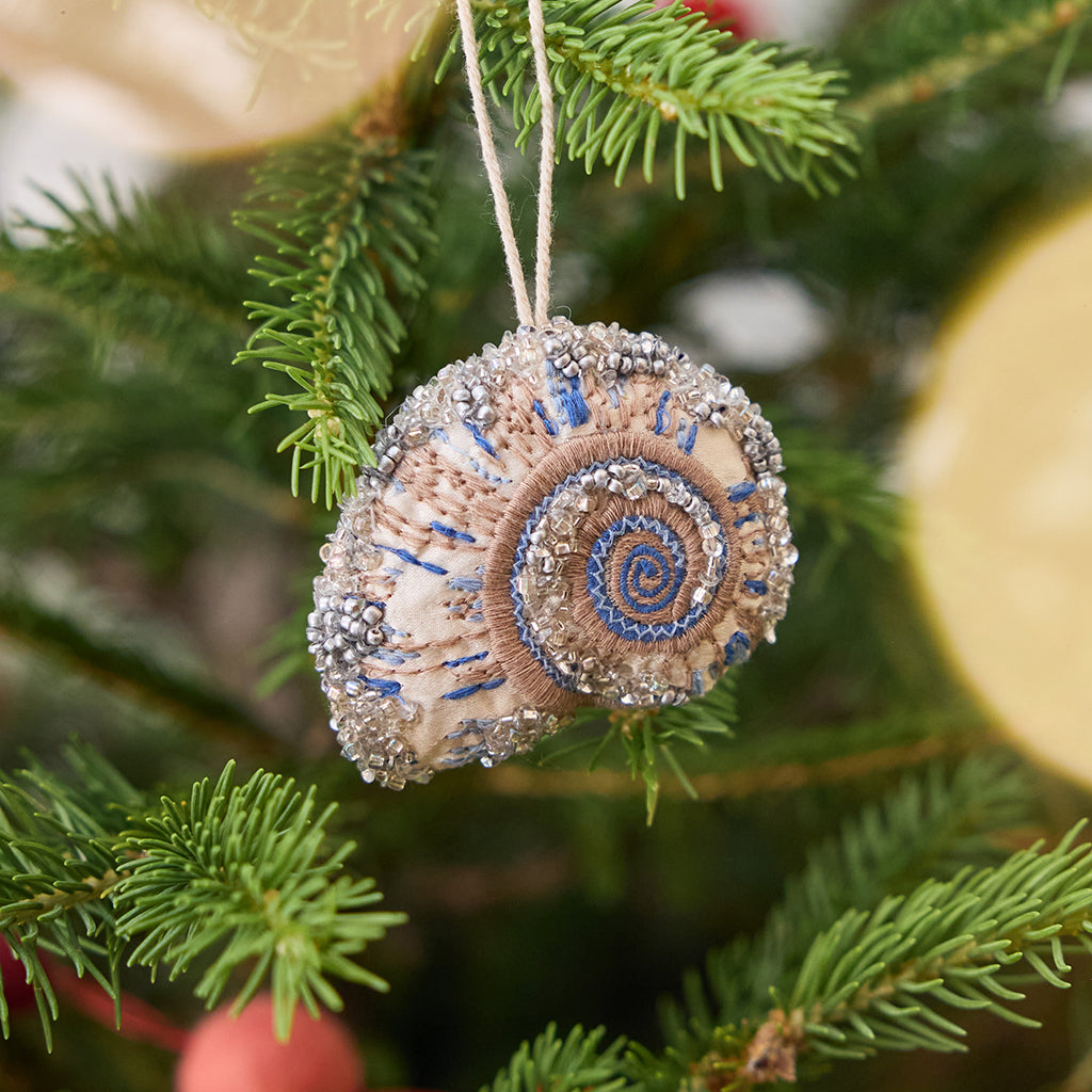 Craftspring’s Moon Snail Shell Ornament displayed on a Christmas tree — made of satin with intricate beaded and embroidered details, adding coastal holiday charm and gifting warmth, ethically crafted by artisans.