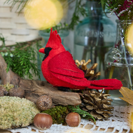 Craftspring’s handmade felt Cardinal ornament — featuring delicate beaded and embroidered details, displayed perched on a stick surrounded by acorns, moss, and pinecones for a cozy woodland holiday scene, perfect for Christmas decorating or gifting, ethically crafted by artisans using sustainable wool.
