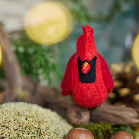 Craftspring’s handmade felt Cardinal ornament — featuring delicate beaded and embroidered details, displayed perched on a stick surrounded by acorns, moss, and pinecones for a cozy woodland holiday scene, perfect for Christmas decorating or gifting, ethically crafted by artisans using sustainable wool.