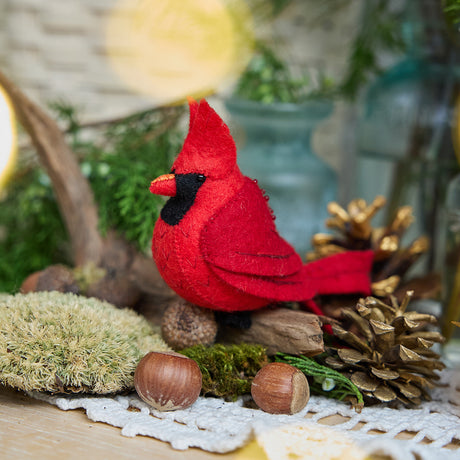 Craftspring’s handmade felt Cardinal ornament — featuring delicate beaded and embroidered details, displayed perched on a stick surrounded by acorns, moss, and pinecones for a cozy woodland holiday scene, perfect for Christmas decorating or gifting, ethically crafted by artisans using sustainable wool.