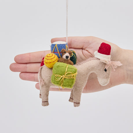 Handmade felt Donkey with Gifts ornament from Craftspring held in front of a hand to show its size—featuring a Santa hat and detailed toys on its back, showcasing heirloom-quality Christmas decor, ethically crafted by artisans using sustainable wool.