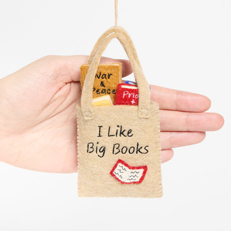 Handmade felt ornament shaped like a tote bag filled with miniature felt books, including titles like Pride & Prejudice and War & Peace. Crafted from soft merino-blended wool, this quirky ornament is a playful nod to literary humor. Perfect for bookworms, teachers, librarians, and pun enthusiasts, it adds a clever touch to holiday trees, bookshelves, or classrooms. Ready to hang with a string attached. Scale sizing reference