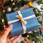 Craftspring’s smallest blue gift box wrapped with twill ribbon, held in hand to show its size—high-quality packaging for holiday gifting, ethically crafted by artisans with care and perfect for heirloom Christmas felt decor.