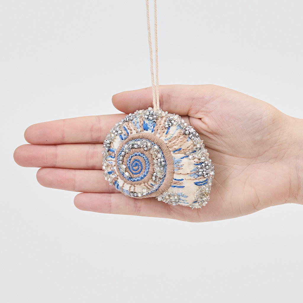 Craftspring’s Moon Snail Shell Ornament displayed in front of a hand to show its size — made of satin with intricate beaded and embroidered details, ethically crafted by artisans.
