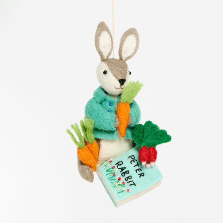 Handmade wool ornament of Peter Rabbit, featuring the beloved children's book character sitting with a carrot in one paw and an embroidered book on his lap. He wears his signature blue jacket, crafted with detailed stitching. Made from natural felted merino-blend wool, the ornament is ready to hang and sized approximately 4.5 inches tall. GIF 360 degree view.