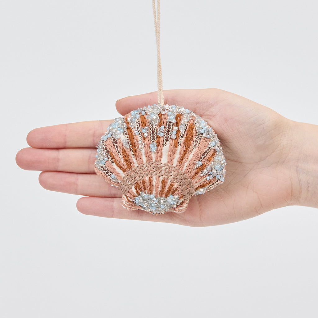 Craftspring’s Scallop Shell Ornament displayed in front of a hand to show its size — made of satin with intricate beaded and embroidered details, ethically crafted by artisans.