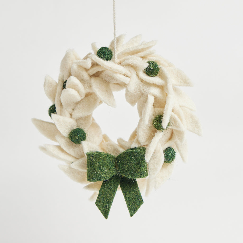 A handcrafted white holiday wreath ornament with green berries and a green bow, ready to hang.