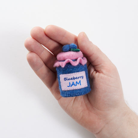 Hand-felted blueberry jam jar ornament with a gingham-style lid and a bunch of plump felt blueberries on top. Made from merino-blend wool, this 3-inch tall ornament is a charming, summer-inspired gift for bakers and brunch lovers. Perfect for cottagecore décor, holiday trees, or breakfast-themed bundles. In a hand for scale reference.