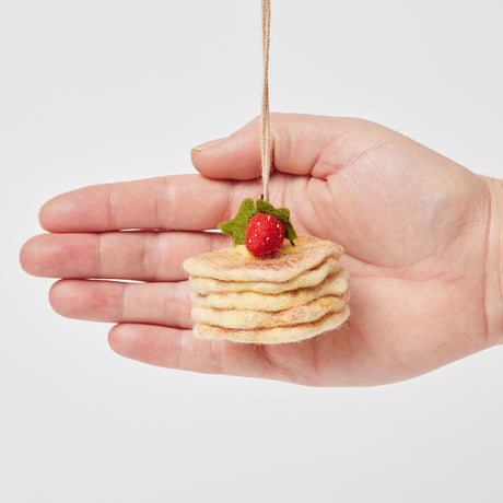 Hand-felted ornament featuring a stack of golden-brown pancakes topped with red strawberries and a square of butter. Made from natural merino-blend wool, this 1.75-inch tall breakfast-themed decoration is perfect for foodies, brunch lovers, and cozy summer gifting. Hand for scale reference