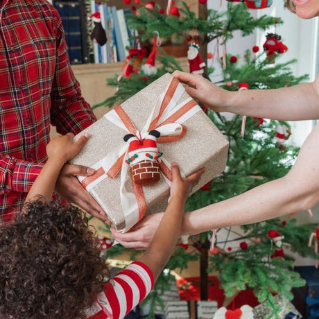 a family moment by the tree, gifting a beautifully wrapped gifts, topped with a felt gift topper, 