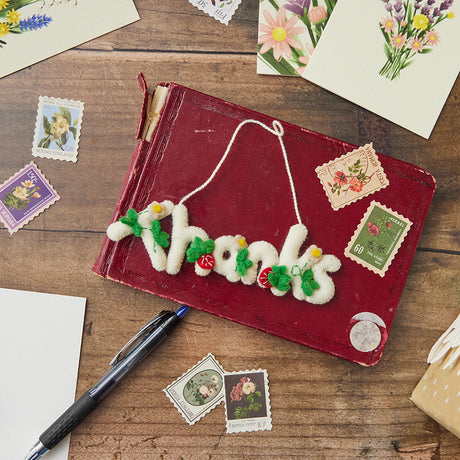 Handmade felt Christmas ornament from Craftspring’s Retirement Collection, featuring the word ‘Thanks’ adorned with sweet strawberries—heirloom-quality holiday decor, ethically crafted by artisans in Kyrgyzstan and India using sustainable wool.