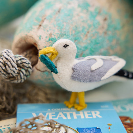 Handmade felt seagull ornament from Craftspring’s Coastal Maine Collection, holding a fish in its beak and displayed among lobster buoys—heirloom-quality Christmas decor, ethically crafted from sustainable wool.