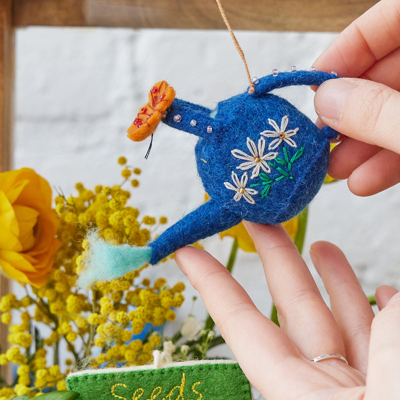 Handcrafted felt watering can ornament with butterfly, floral embroidery, and beaded garden details