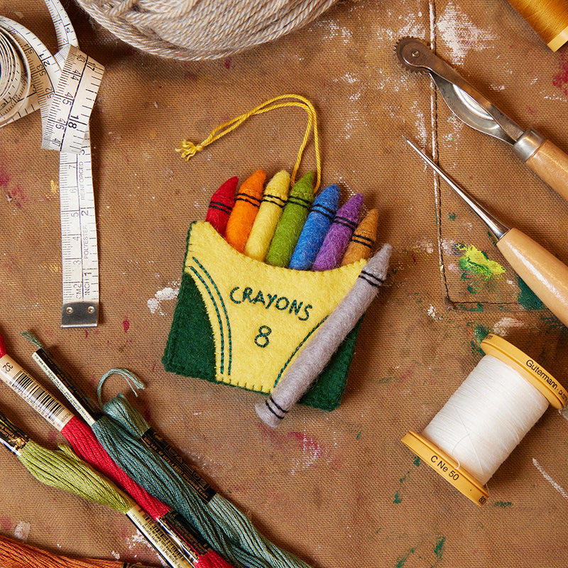 Hand-felted crayon box ornament with colorful stitched crayons, celebrating creativity, teaching, and childhood imagination. Handmade and fair trade.

