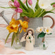 Handmade felt daisy flower bouquet with five white and yellow blooms in a recycled handblown glass vase. Eco-friendly spring décor or gift for Mother's Day, teachers, or Easter. Fair trade and sustainably crafted. Featured with a felt angel and daffodil bouquet
