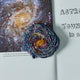 Round galaxy ornament with beaded stars and spiral design, handmade on satin fabric.


