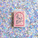 Hot pink felt ornament shaped like a small book, featuring delicately embroidered open pages. Inspired by the beloved Brooklyn bookstore Books Are Magic, this hand-felted wool ornament includes a hanging string and measures approximately 2.5 inches tall. A colorful tribute to the joy of reading and storytelling