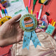 Handmade felt reading badge shaped like a ribbon with shimmering star details, designed to celebrate young readers' achievements. Crafted from merino-blended wool, the badge comes pinned to an illustrated postcard with space for a personal message, and includes an envelope for gifting. Features both a safety pin and a hanging loop. A fun, motivational keepsake for children, perfect for classrooms, libraries, or reading milestones.