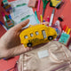 Yellow school bus ornament handcrafted from felted wool, featuring red stitched lights and fair trade craftsmanship. Ideal for teacher gifts and classroom décor.

