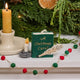 Miniature hand-felted wool ornament shaped like an open book titled A Christmas Carol, featuring embroidered details including a writing plume and a golden chamberstick. Crafted from merino-blend wool with a hanging string, the ornament evokes Victorian charm and the classic story of Ebenezer Scrooge. Measures approximately 2.25 inches high and 3.75 inches wide.