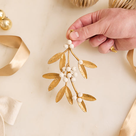 Add a little holiday romance to the tree with our Mistletoe Metal Ornament. Inspired by vintage botanical decorations, this delicate golden mistletoe is beautifully handcrafted with embossed iron leaves, hand-cast resin details, and a softly aged gilt finish.