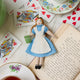 Hand-felted wool ornament of Alice from Alice in Wonderland, wearing her classic blue and white dress and holding a felt copy of Lewis Carroll's book. Crafted with embroidered details and made from merino-blend wool, the ornament includes a hanging string and measures approximately 5.75 inches tall