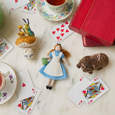 Set of three hand-felted wool ornaments inspired by Alice in Wonderland, including Alice in her blue dress holding a book, the grinning Cheshire Cat with black stripes, and the Caterpillar sitting on a mushroom with a hookah and the phrase 'Who are you?' stitched below. Each ornament features detailed embroidery, includes a hanging string, and is handmade from merino-blend wool.