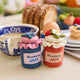 Hand-felted wool ornament of a strawberry and blueberry jam jar, topped with a white gingham-style lid and a blooming felt strawberry. Features a stitched label and vibrant red detailing, evoking homemade summer preserves. Measures 3.25 inches tall and includes a hanging string — a charming gift for gardeners, bakers, or lovers of nostalgic, handmade summer treasures.