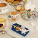 Hand-felted ornament of a floral teacup with a matching saucer, featuring embroidered golden rims, a tiny felt tea bag, and two sugar biscuits on the side. Around the tea cup are other ornaments in the tea collection. Crafted from merino-blend wool with fine needlework, the ornament includes a hanging string and measures approximately 1.5 inches high and 3.25 inches wide. A charming tribute to afternoon tea and cozy traditions.
