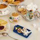 Handcrafted felt ornament of an embroidered tea tray topped with finger sandwiches, pastries, and a small bouquet of flowers. Made from merino-blend wool with soft textures and fine stitching, this ornament includes a hanging string and measures approximately 1.25 inches high and 3.75 inches wide. A charming nod to English tea parties and cozy mornings.