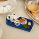 Handcrafted felt ornament of an embroidered tea tray topped with finger sandwiches, pastries, and a small bouquet of flowers. Made from merino-blend wool with soft textures and fine stitching, this ornament includes a hanging string and measures approximately 1.25 inches high and 3.75 inches wide. A charming nod to English tea parties and cozy mornings.