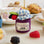 Hand-felted wool ornament of a berry jam jar with a red gingham-patterned lid, topped with beaded blackberry and raspberry accents. Crafted with embroidered details and soft textures, it includes a hanging string and measures approximately 2.75 inches high. A sweet, handmade tribute to homemade preserves and cozy kitchen moments.