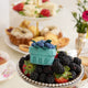 Felt blueberry pint ornament with hand-felted blue berries in a soft green wool basket sitting on top of a bowl of fresh berries. Handmade from natural wool felt using traditional needle-felting. Fair trade and ready to hang.