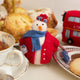 Felt snowlady ornament wearing a red coat and fascinator, holding a teacup and blue handbag. Handmade from wool felt using traditional needle-felting. Fair trade and ready to hang.