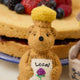 Hand-felted ornament of a golden bear shaped like a classic honey jar, featuring a sparkling beaded finish and an embroidered clover on its chest. Inspired by Winnie the Pooh, this merino-blend wool ornament includes a hanging string and measures approximately 4.5 inches tall. A sweet, handmade tribute to childhood memories and the magic of the Hundred Acre Wood. 