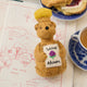 Hand-felted ornament of a golden bear shaped like a classic honey jar, featuring a sparkling beaded finish and an embroidered clover on its chest. Inspired by Winnie the Pooh, this merino-blend wool ornament includes a hanging string and measures approximately 4.5 inches tall. A sweet, handmade tribute to childhood memories and the magic of the Hundred Acre Wood.