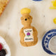 Festive hand-felted wool ornament of a honey bear jar, sparkling with beaded details and a stitched clover on its chest. Inspired by Winnie the Pooh, this cozy golden bear makes a charming holiday gift and nostalgic keepsake. Includes a hanging string and measures approximately 4.5 inches tall — perfect for tree decorating, gift-topping, or stocking stuffing.