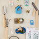 Miniature birdhouse ornament handcrafted from felted wool, featuring a cozy stitched design and hanging string—perfect for springtime décor or gifting to bird lovers