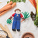 Felt Santa ornament in garden overalls holding a carrot—handcrafted for nature-themed Christmas trees