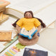 Handmade felt ornament of a young girl sitting cross-legged, absorbed in a book. Crafted from natural merino-blended wool, her focused gaze and relaxed posture capture the magic of reading. With braided brown hair and a warm-toned complexion, this ornament adds a cozy, literary touch to reading nooks, desks, or shelves. A perfect gift for bookworms, young readers, or anyone who treasures the quiet joy of a good story. Ready to hang with a string attached.