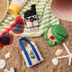 Handmade felt summer ornaments from Craftspring, featuring a beach bag, retro Polaroid camera, and turtle-shaped sandbox—displayed on a sandy shore with seashells, sunglasses, and a beach towel for a whimsical seaside scene, ethically crafted by artisans in India using sustainable wool.