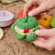 Handmade felt Turtle Sandbox ornament from Craftspring held gently over a sandy beach with children’s beach toys—evoking nostalgic memories of childhood summers and seaside play, ethically crafted by artisans in India using sustainable wool.